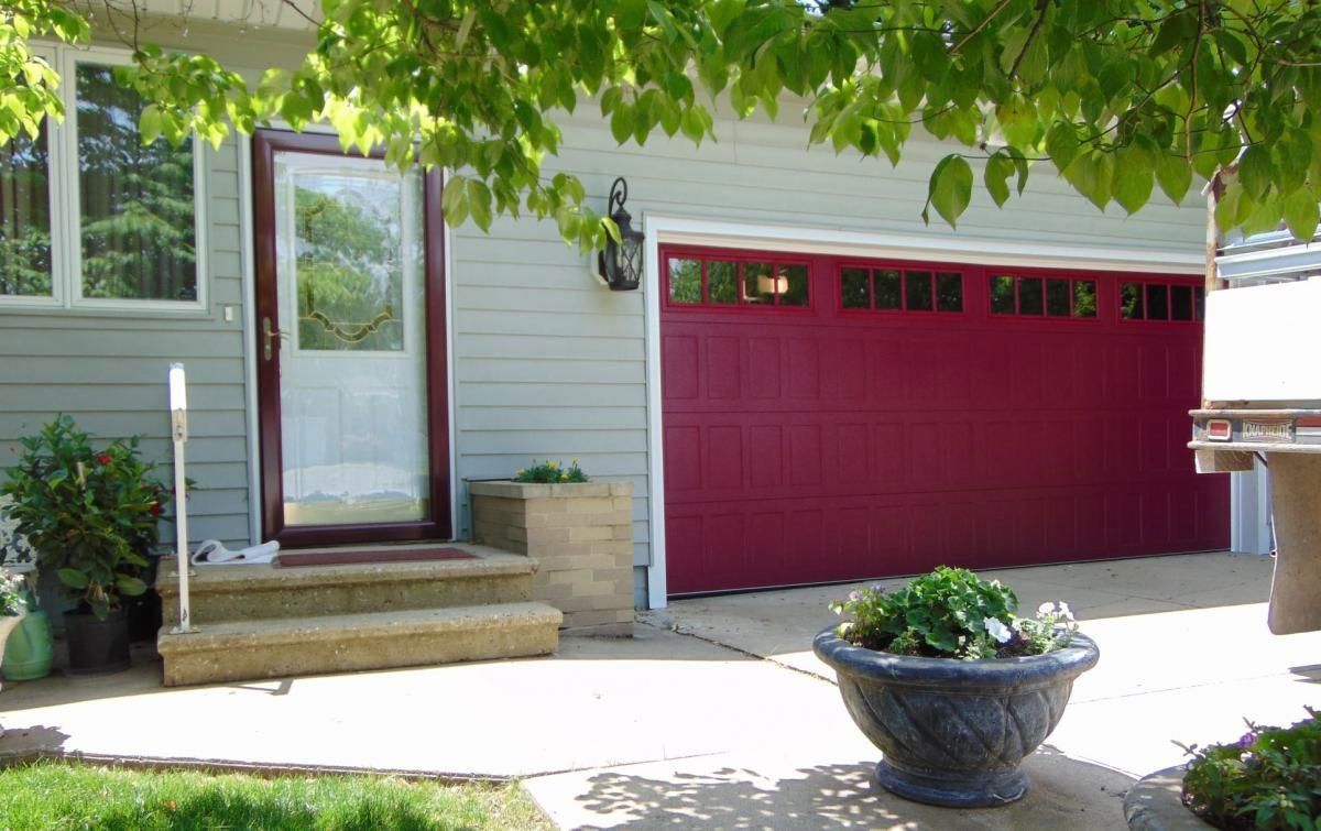 House exterior with red garage door, white siding, front steps, and a potted planter in the driveway