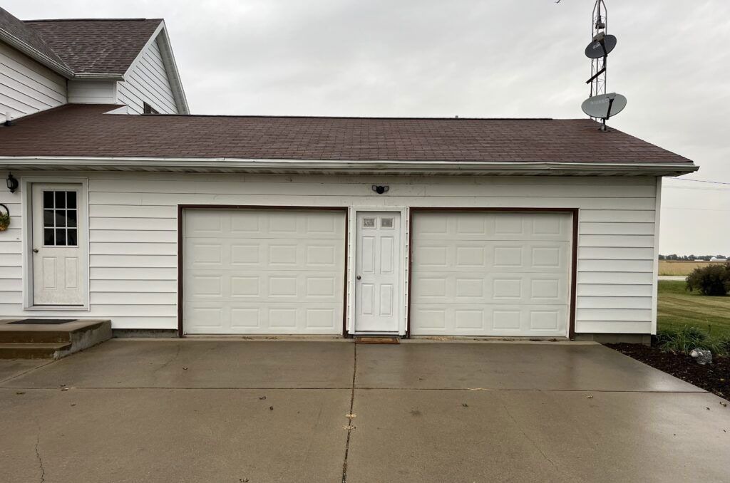 Two-car garage with white doors on a wet driveway beside a house