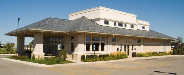 Large modern building with a sloped roof and covered entrance on a paved lot.