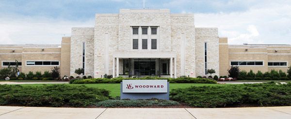 Front view of a white office building with a landscaped entrance and a Woodward sign.