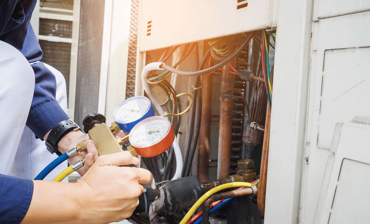 A man is working on an air conditioner with a pressure gauge.