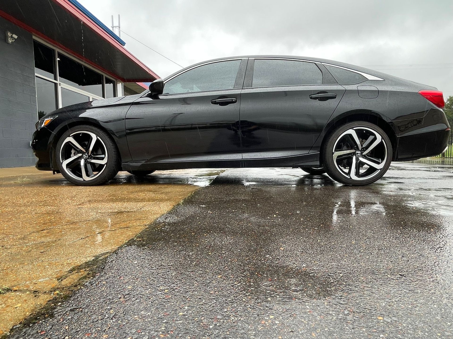 Black sedan parked on wet pavement beside a building.