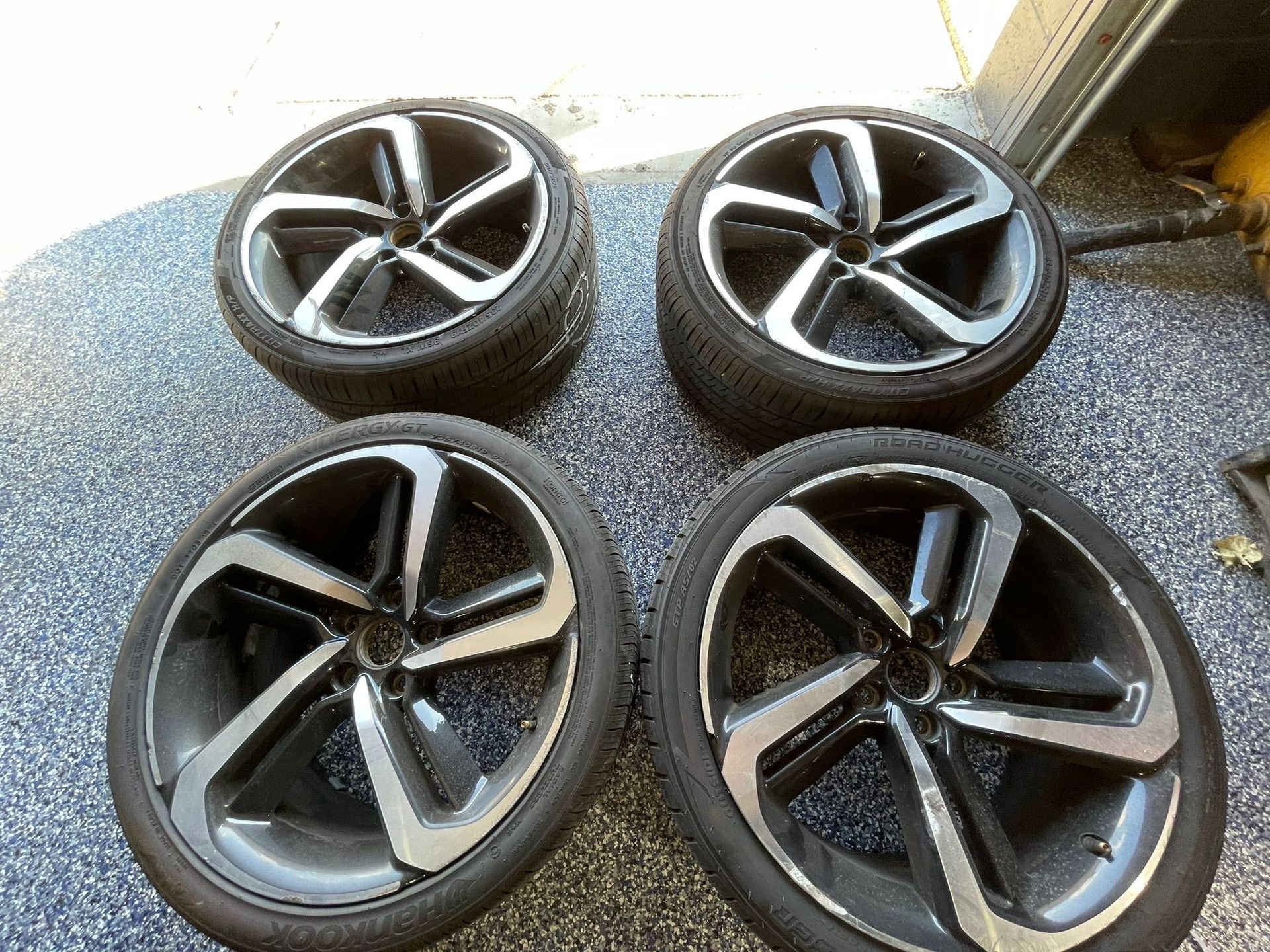 Four black and silver alloy wheels with tires, laying on a patterned surface.