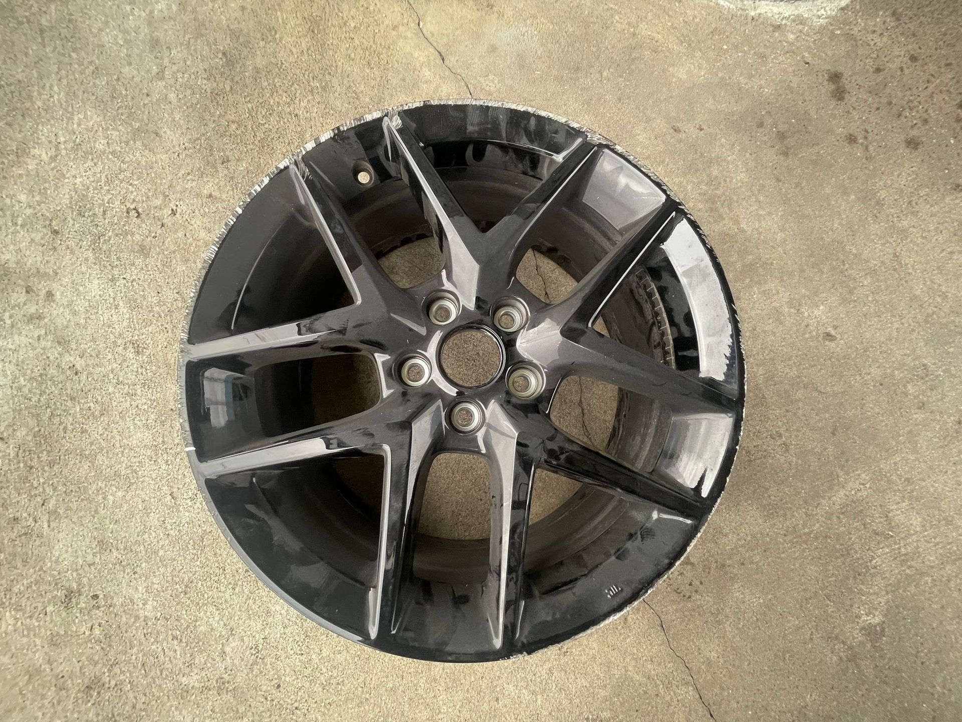 Black alloy car wheel with six spokes, sitting on a concrete surface.