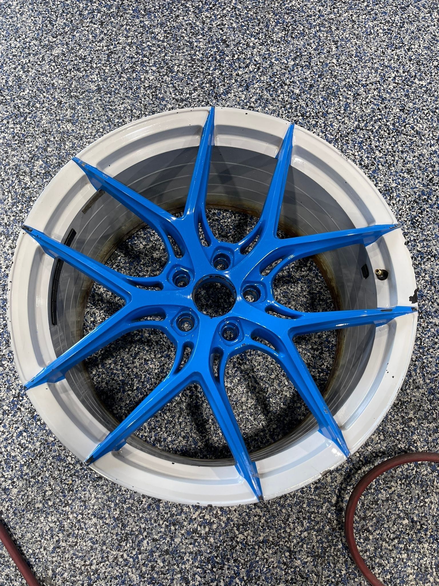 Blue and silver car wheel with star-shaped spokes against a speckled floor.