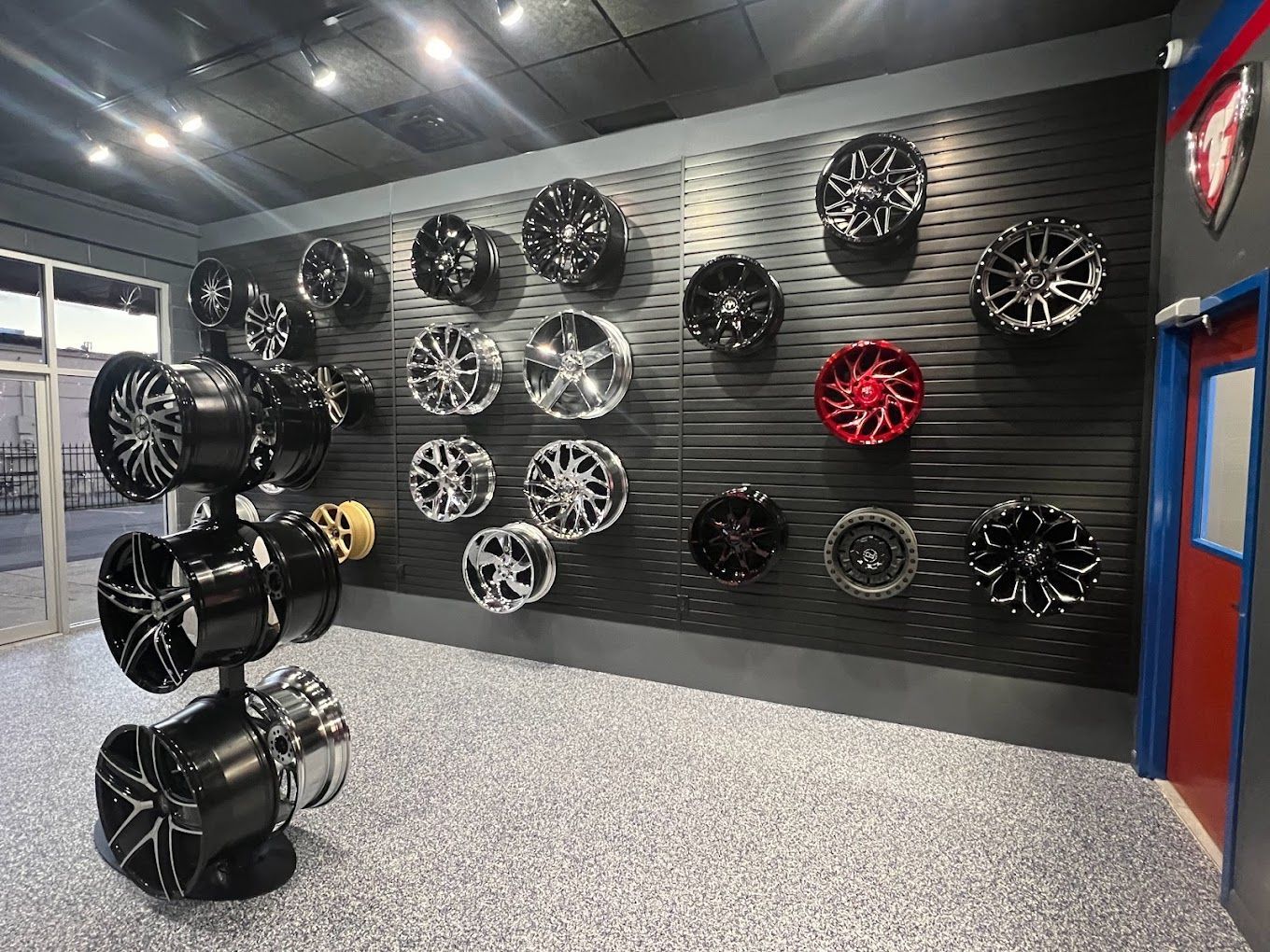Interior of a car accessories shop with rims displayed on a black wall and stacked. Grey speckled floor.