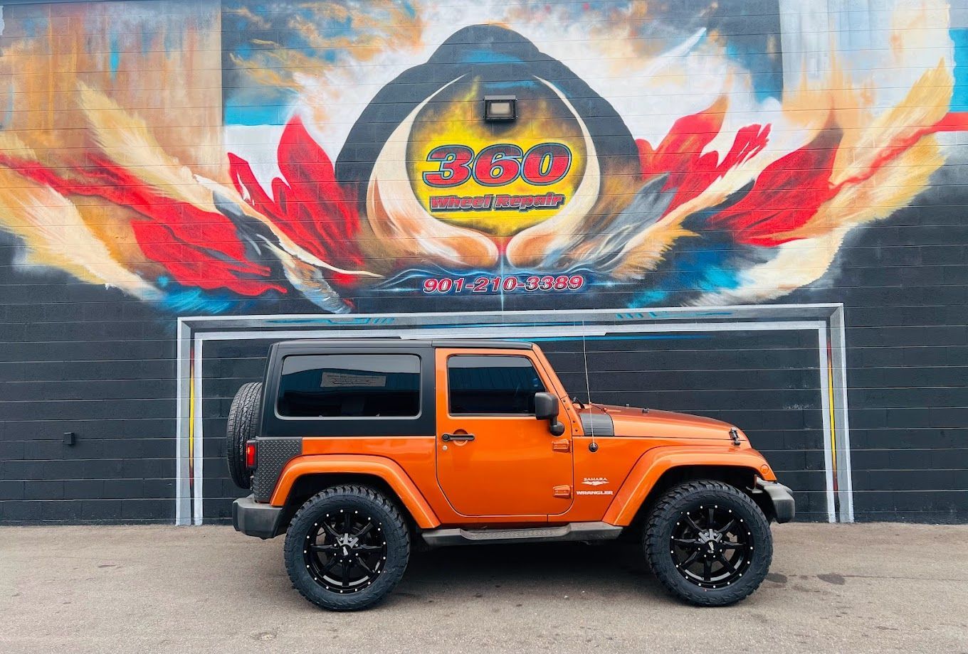 Orange Jeep parked in front of a mural with colorful artwork.