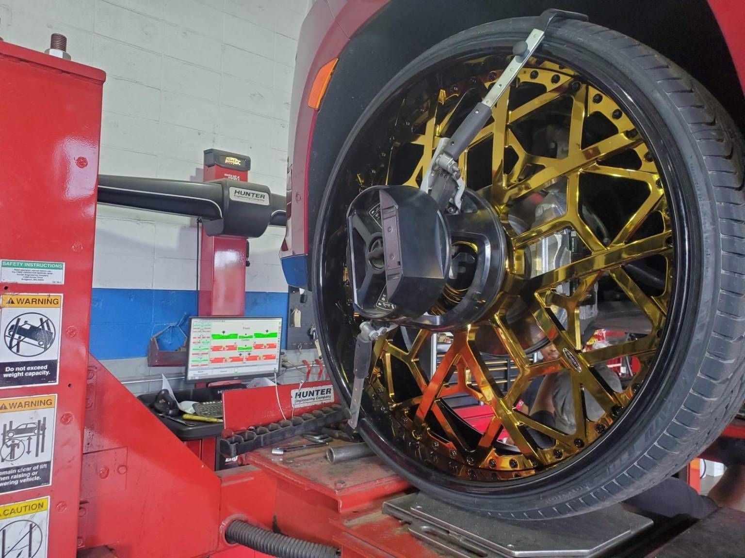 Car wheel with gold spokes being aligned by a machine in a garage.