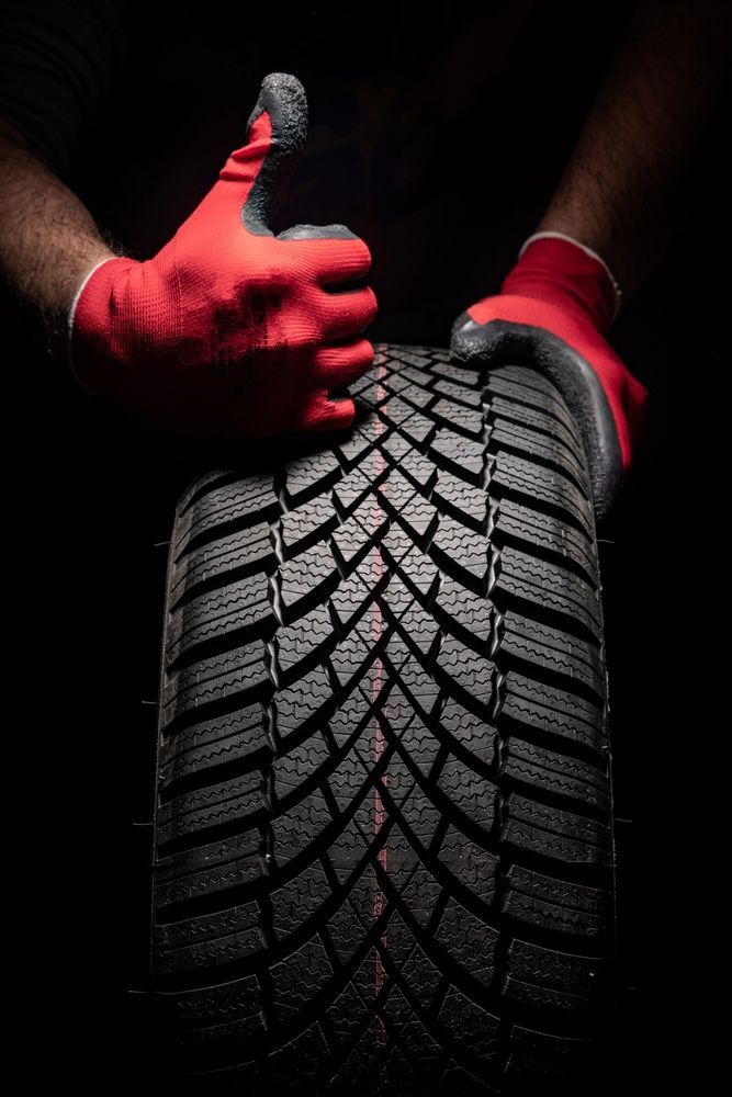 Hands in red gloves holding a tire, one giving a thumbs-up, against a black background.
