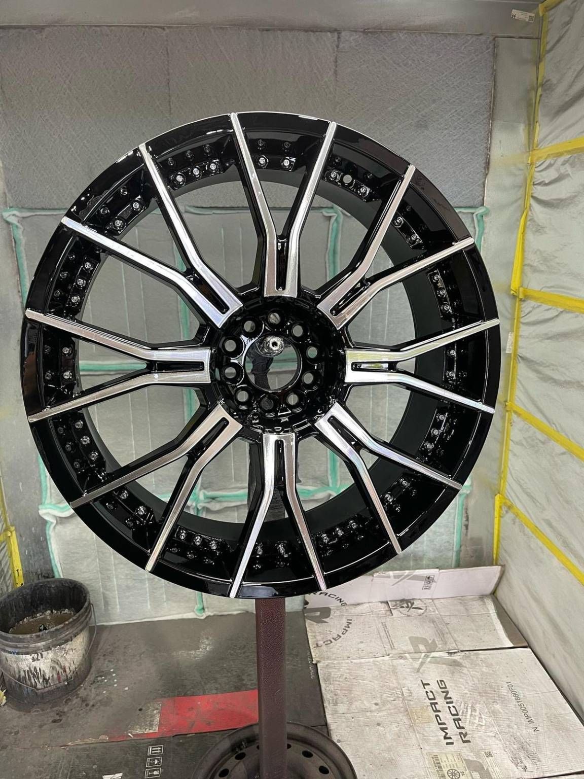 Black and silver car rim on a stand in a spray painting booth.