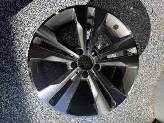 Shiny gray and silver car alloy wheel on a pebbled surface, with six lug nut holes and radiating spokes.