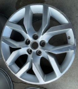 Silver alloy car wheel with five lug nuts and a modern spoke design - before