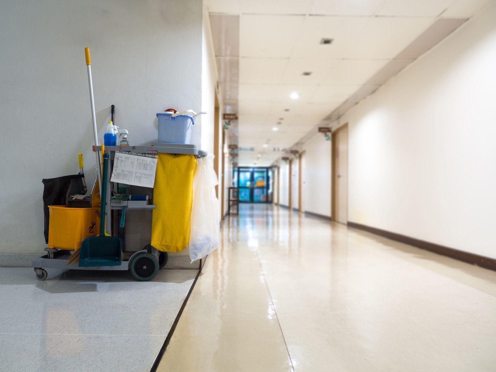 Janitor cart in empty bright hallway with shiny floor and blue doors in the distance
