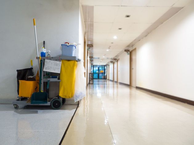 Janitor cart in empty bright hallway with shiny floor and blue doors in the distance