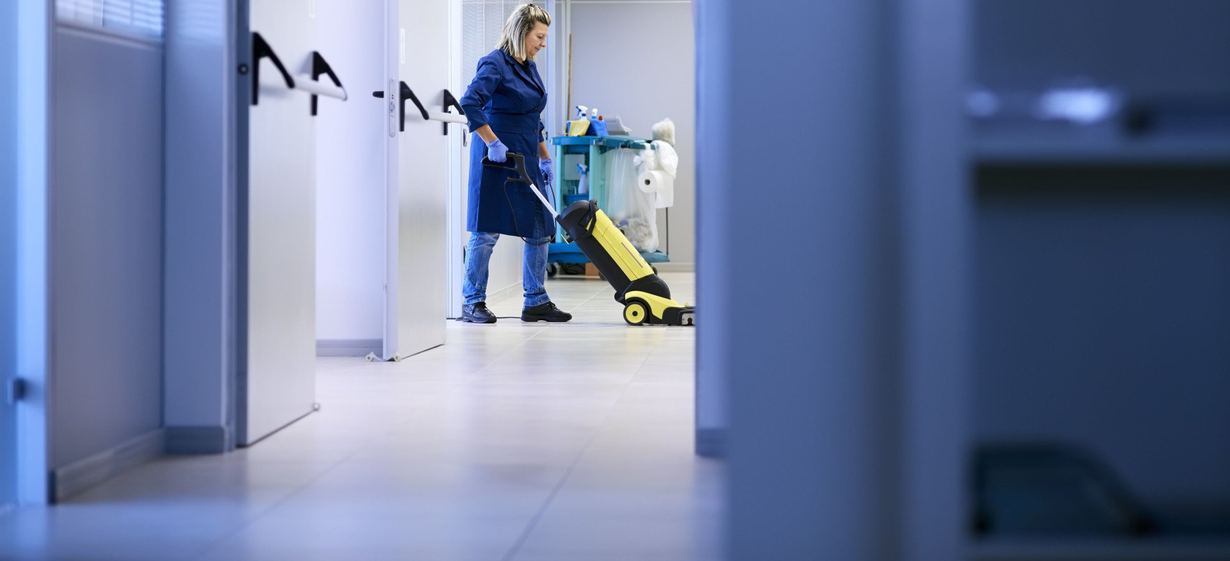 Janitor cleaning a bright hallway with a yellow floor buffer
