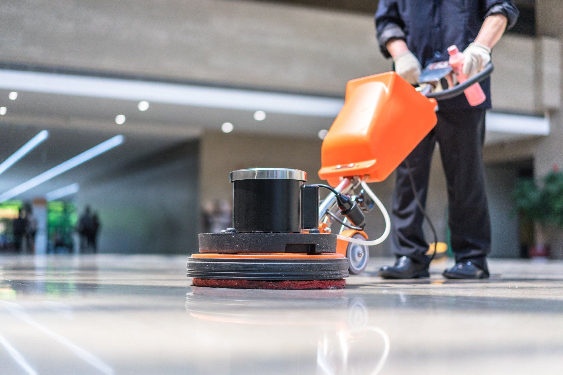 Person using an orange floor buffer on a glossy indoor floor