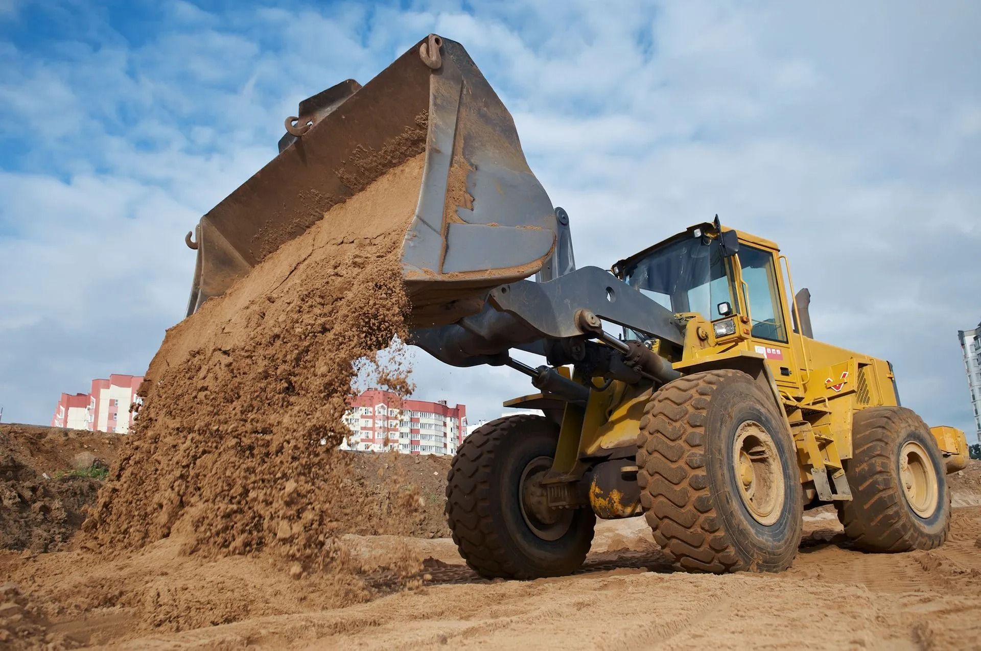 Yellow front loader dumping sand at a construction site