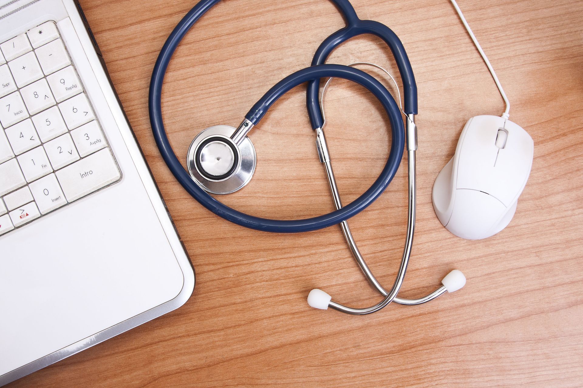 A stethoscope is sitting next to a laptop and mouse on a wooden table.