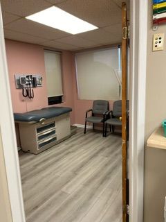 A doctor 's office with a table and chairs and a stethoscope on the wall.