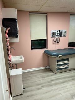 A doctor 's office with a examination table , sink , and window.