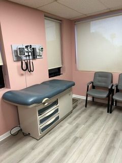 A doctor 's office with a bed , chairs and a stethoscope.