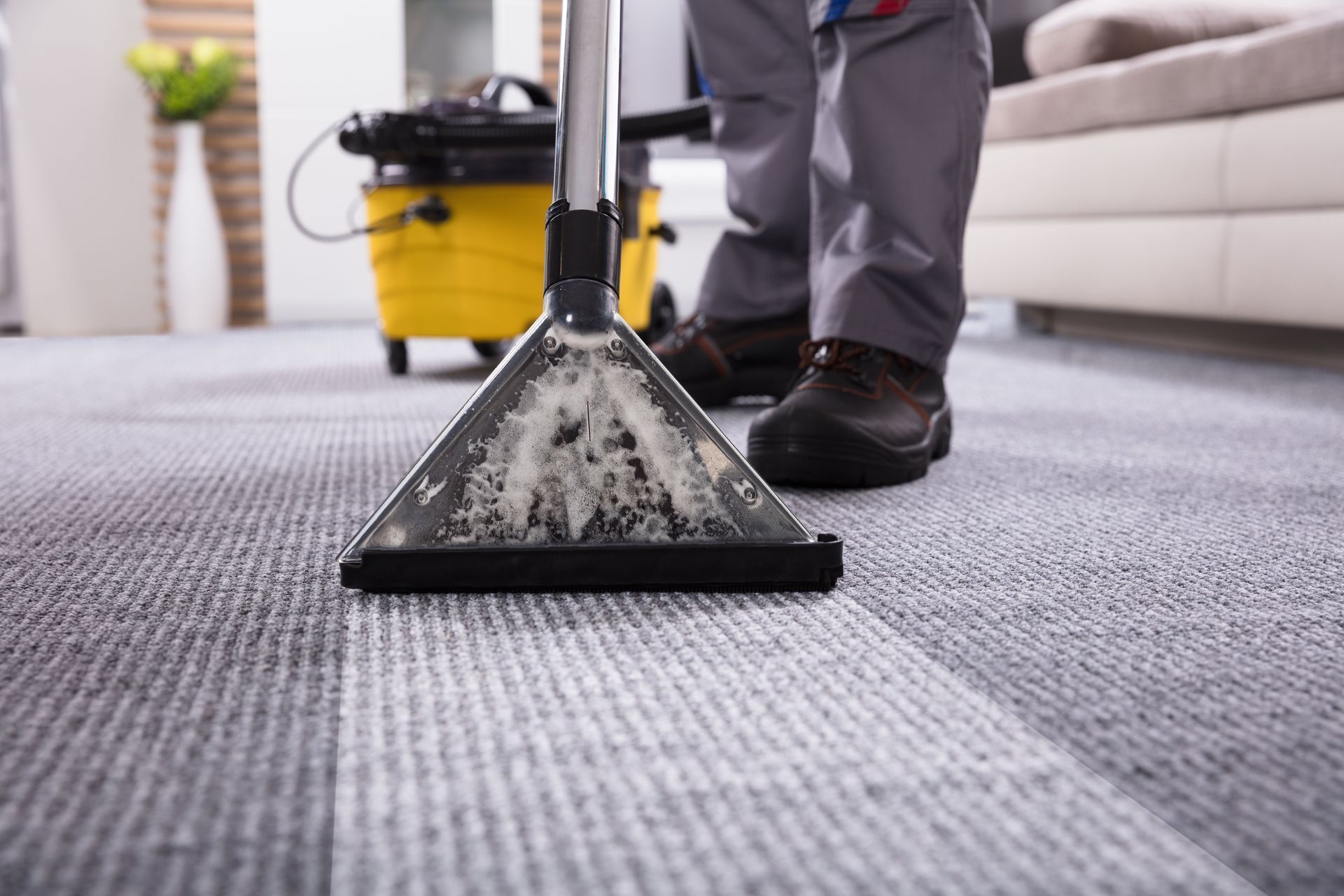 Person cleaning gray carpet with a yellow vacuum cleaner.