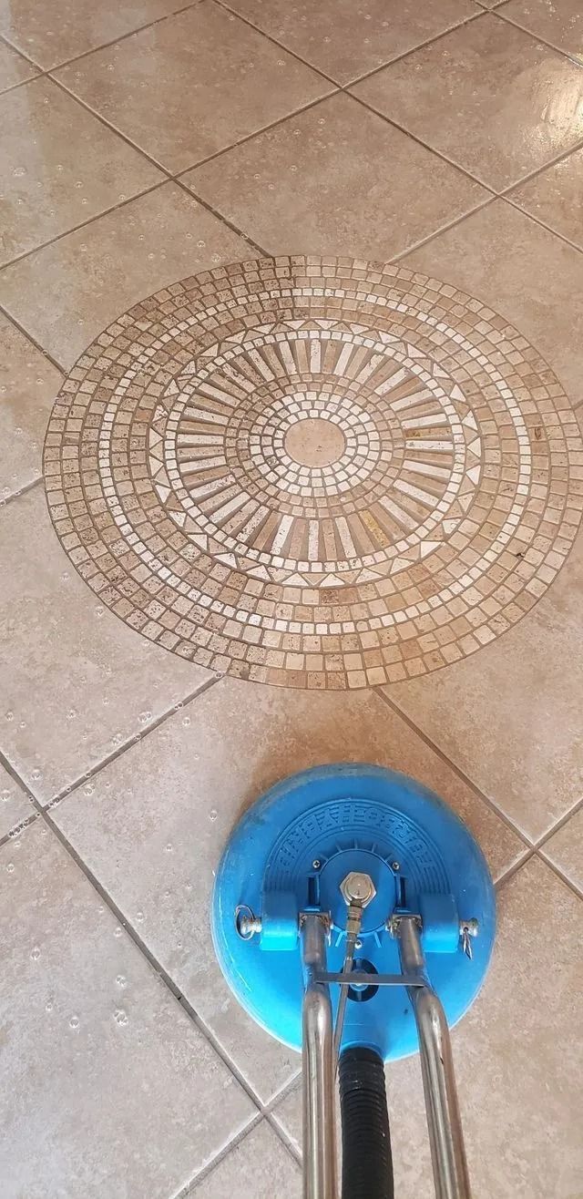 A floor being cleaned with a blue rotary floor cleaner, around a mosaic tile medallion.