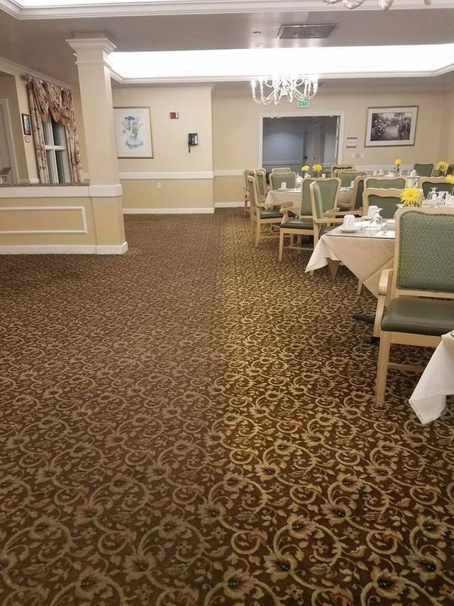 Dining room with tables set for a meal. Carpet has a dark floral pattern, chairs are green.