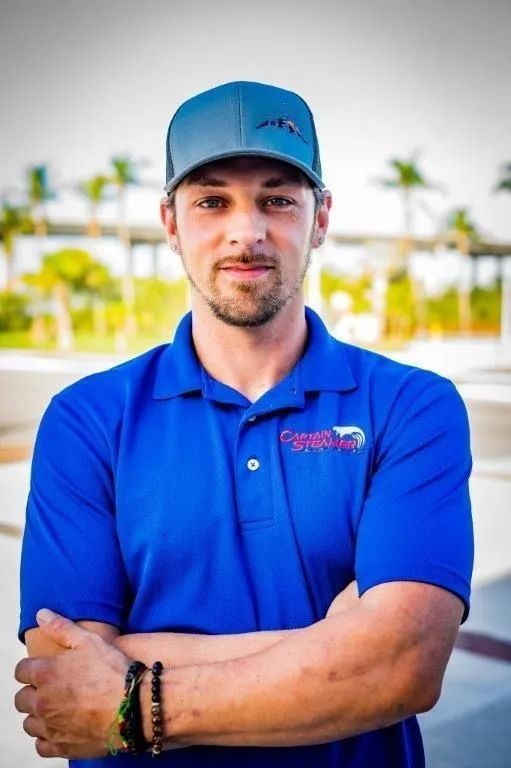 Man in blue polo and cap with arms crossed, standing outdoors.