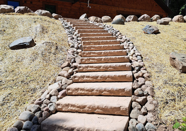 Stone steps lead up a hill to a wooden building, flanked by rocks and grassy patches.