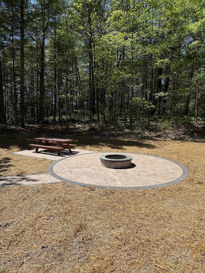 Forest campsite with a picnic table and circular stone fire pit on a gravel clearing