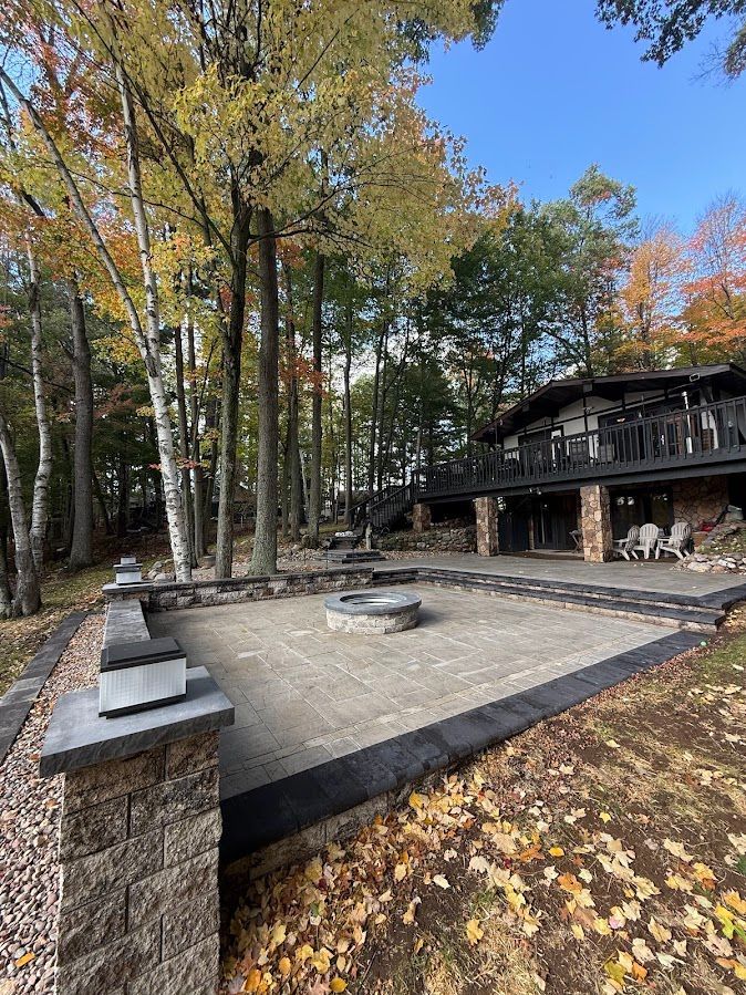 Stone patio with fire pit beside a wooded cabin in autumn.