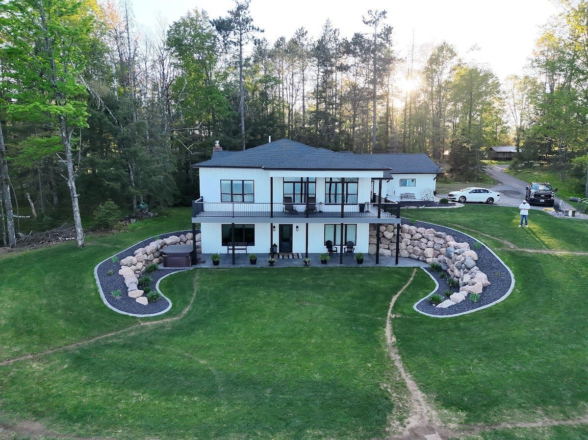 Modern two-story white house on a landscaped lawn, viewed from above at sunset, with trees behind it
