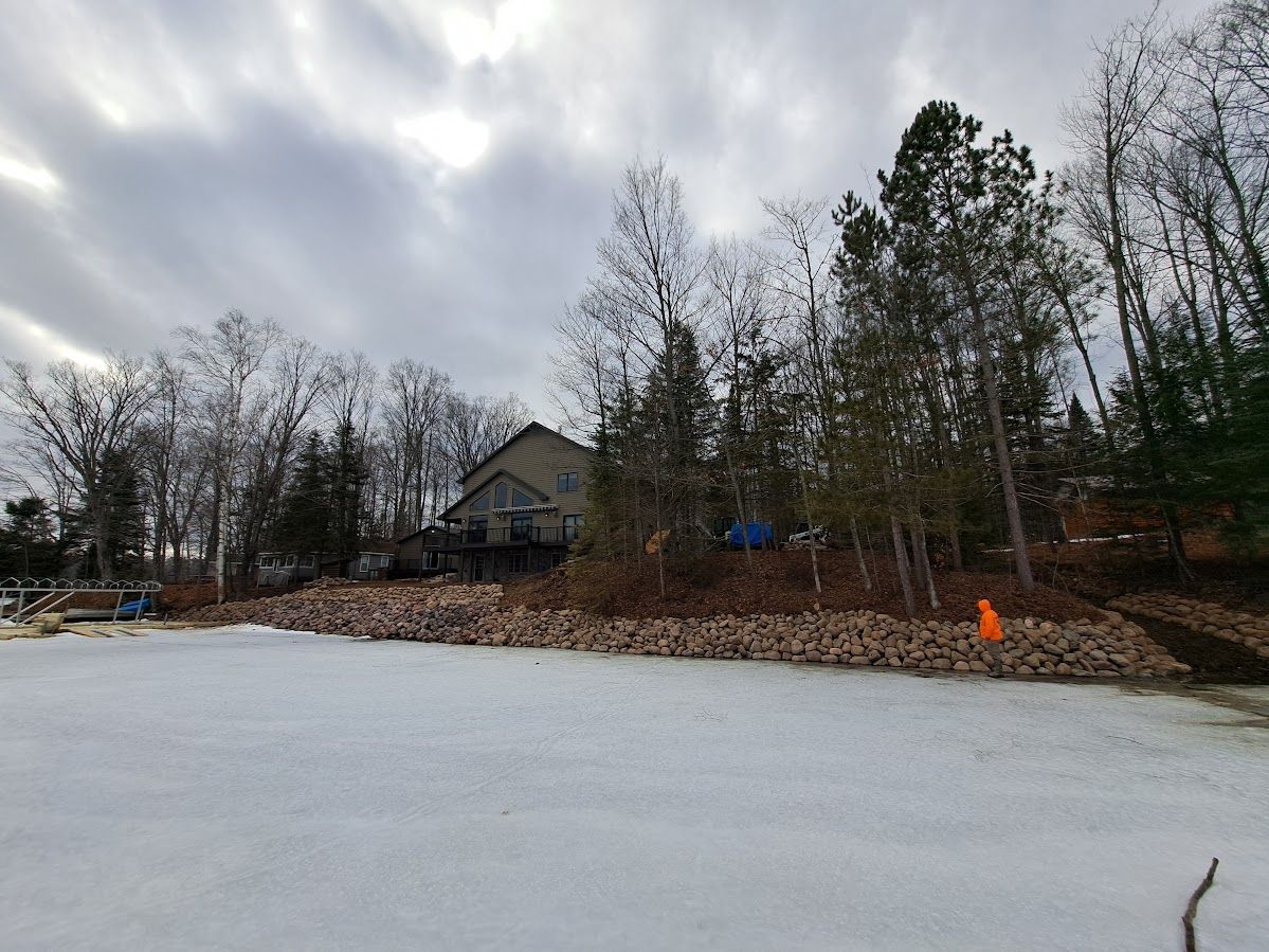 Frozen lake with a house and tall trees under a cloudy sky