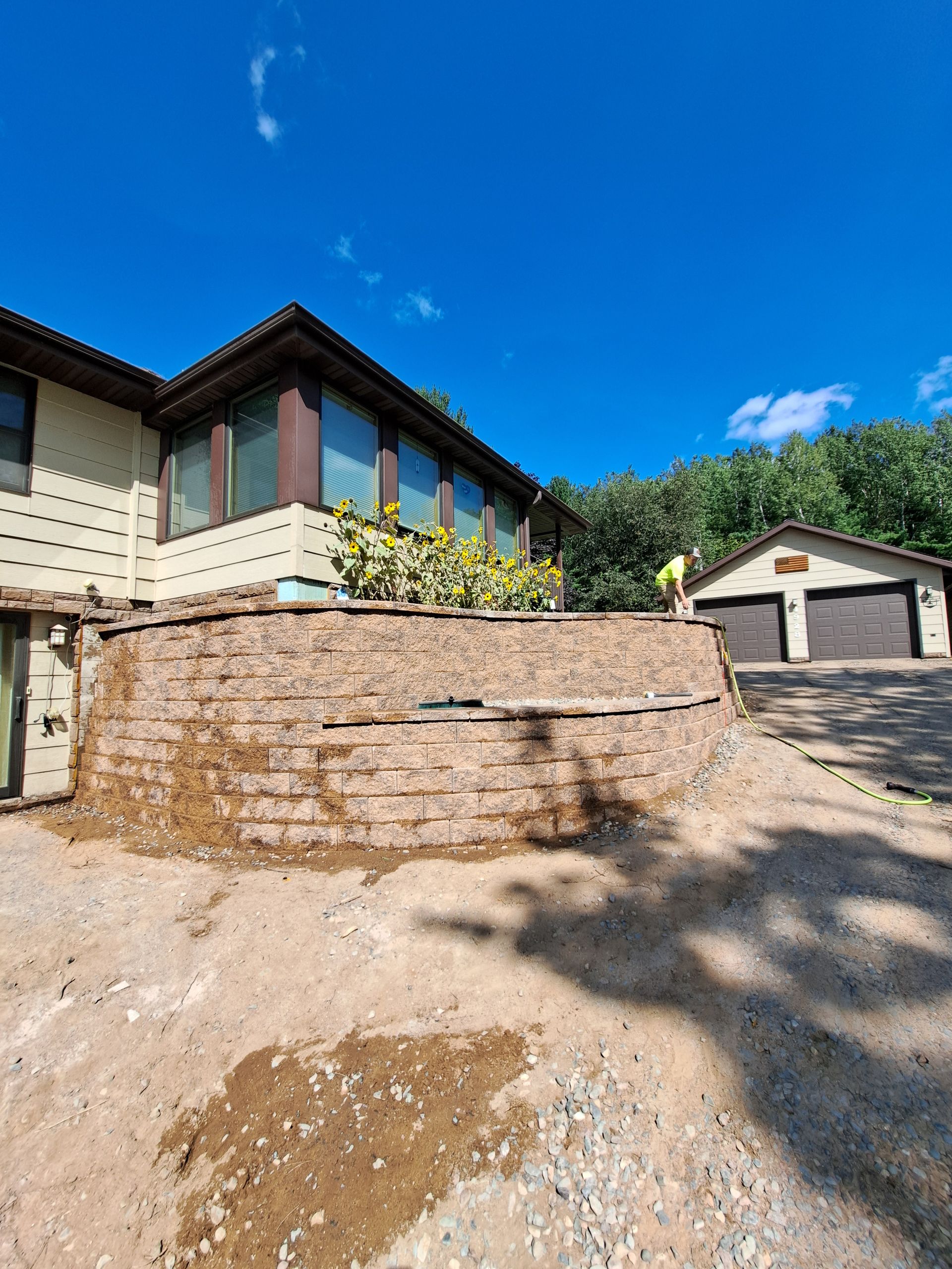 House with retaining wall, garage, and a person working on the wall under a blue sky.