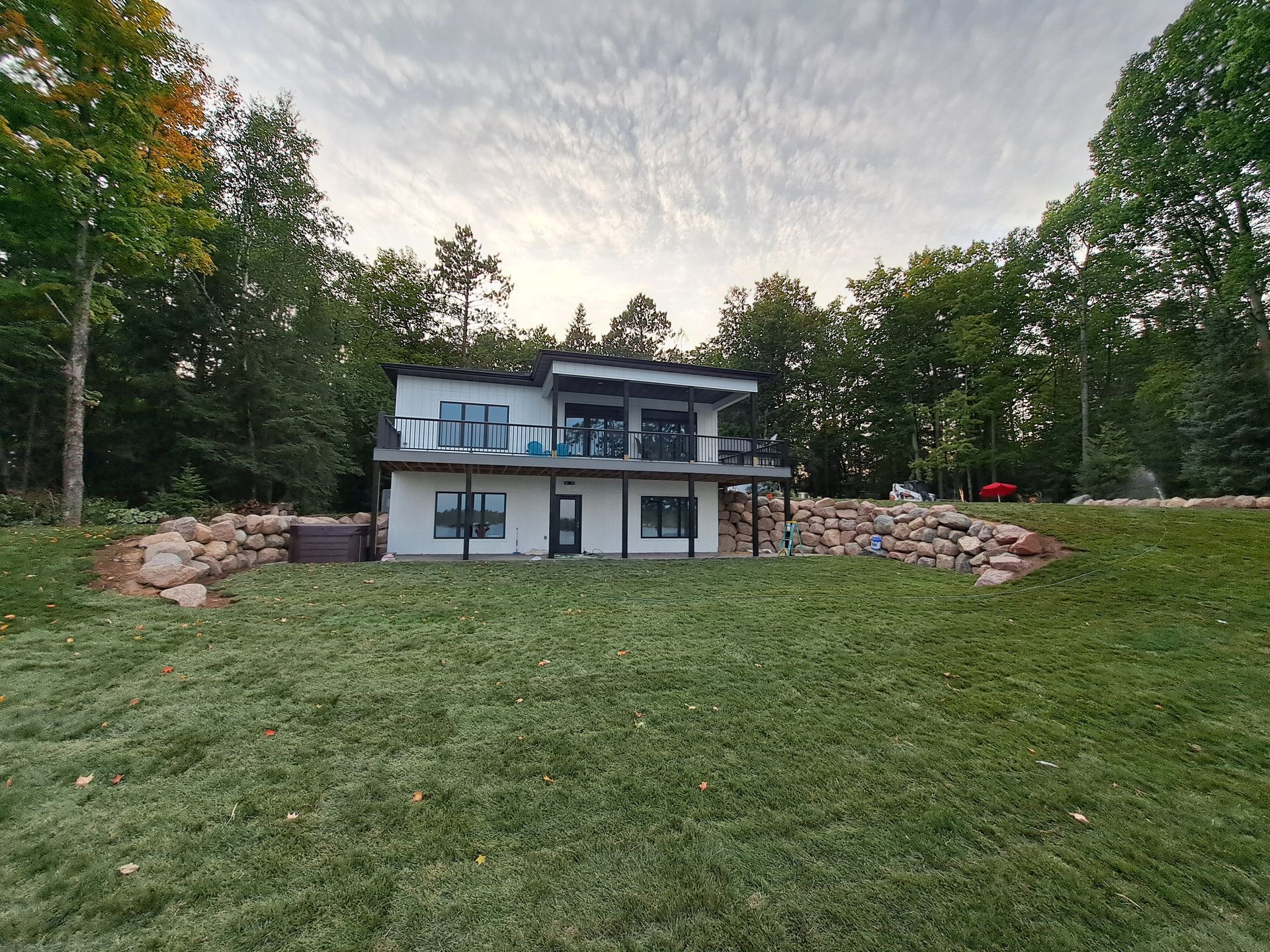 Modern two-story house with black trim, overlooking a grassy lawn and trees.