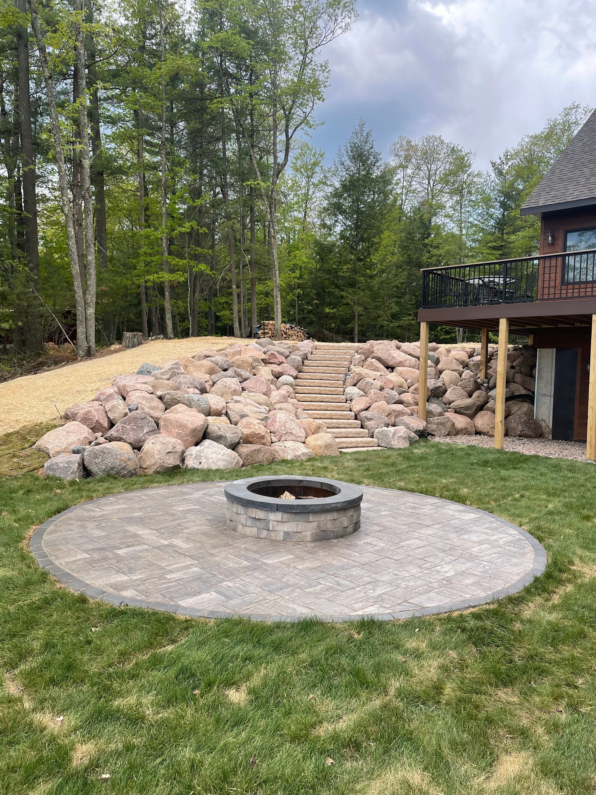 Backyard fire pit area with stone retaining wall and stairs leading up a hill.