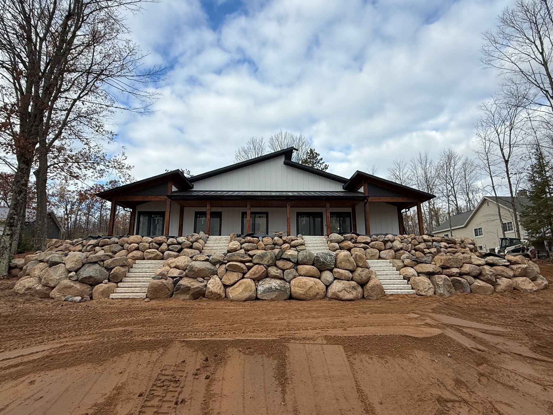 A modern house with a rock retaining wall and steps leading to the entrance under a cloudy sky.