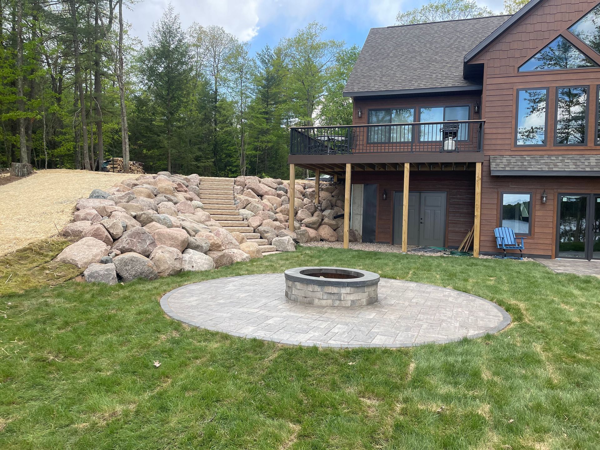 Backyard with fire pit, stone retaining wall, stairs, and house with balcony.