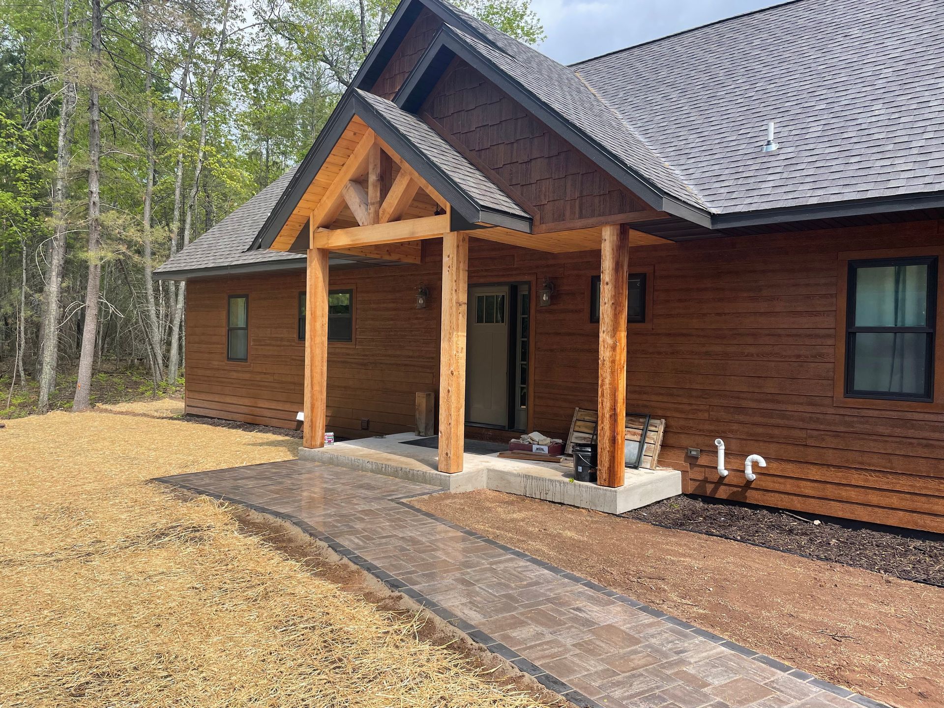 Brown cabin home with a porch, surrounded by gravel and trees.