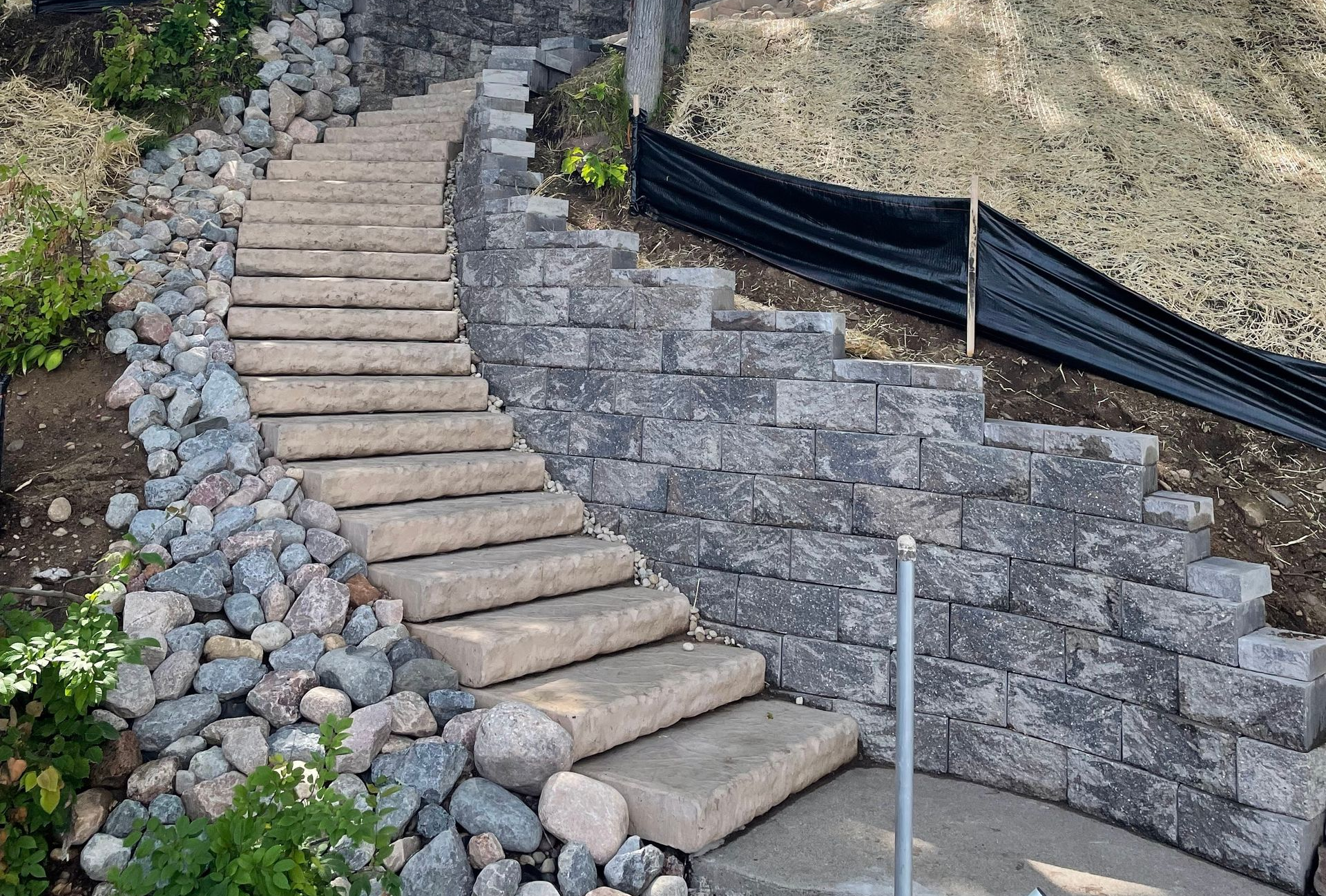 Stone steps ascend a retaining wall on a hillside, with gravel and rocks flanking the staircase.