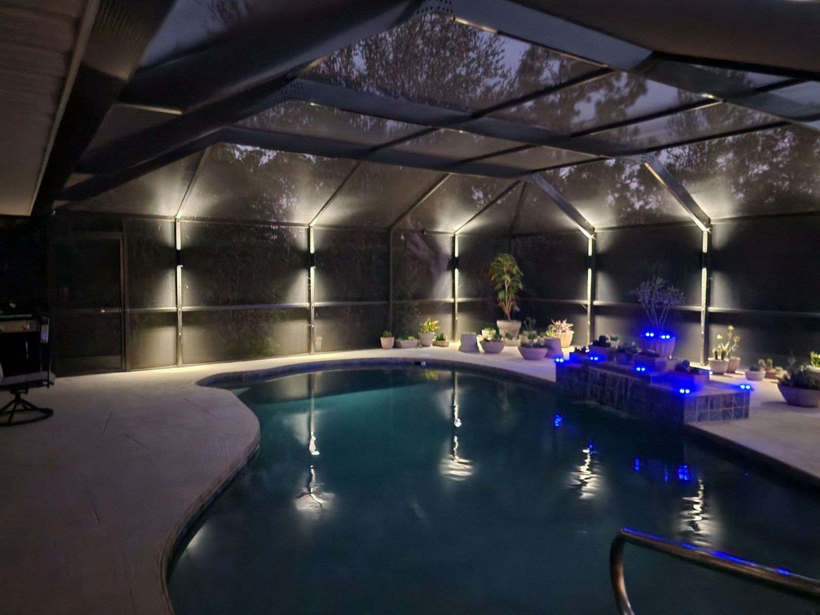 Pool inside screened enclosure with pink flamingo float. Red-tinted windows. Evening lighting.