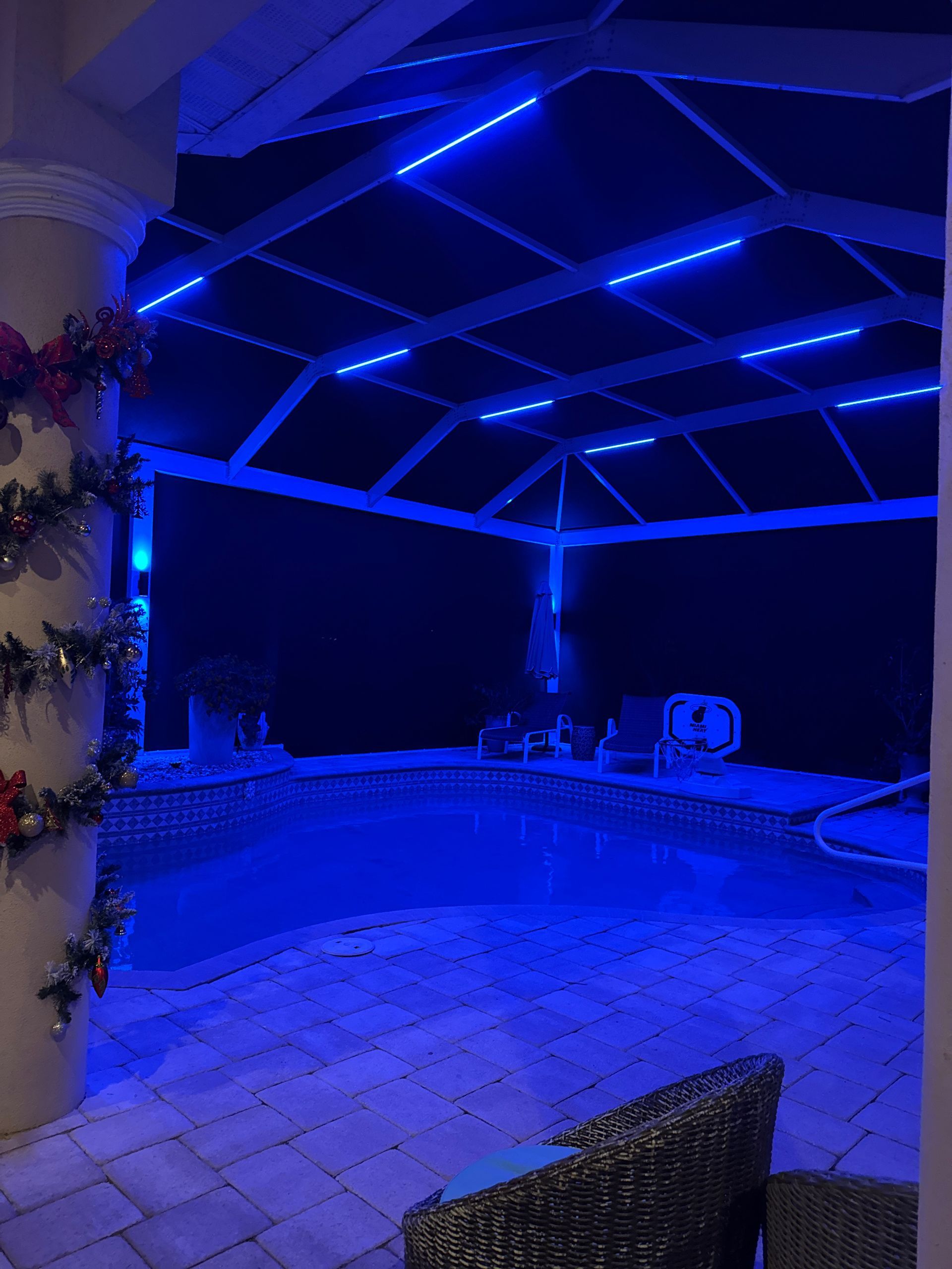 Pool area with blue LED lights. Brick patio, dark water, and decorated columns under a screened enclosure.