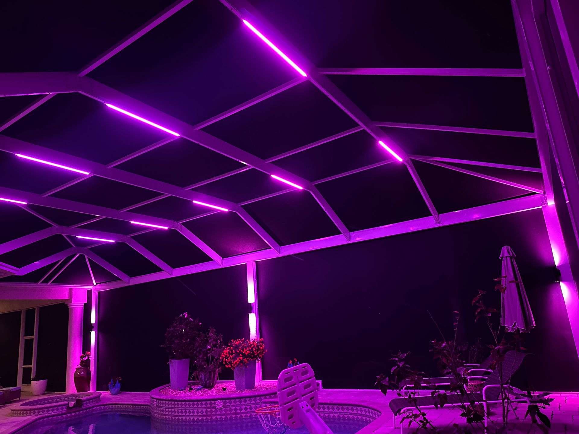 Purple LED lights illuminate a screened-in pool patio roof and structure at night.