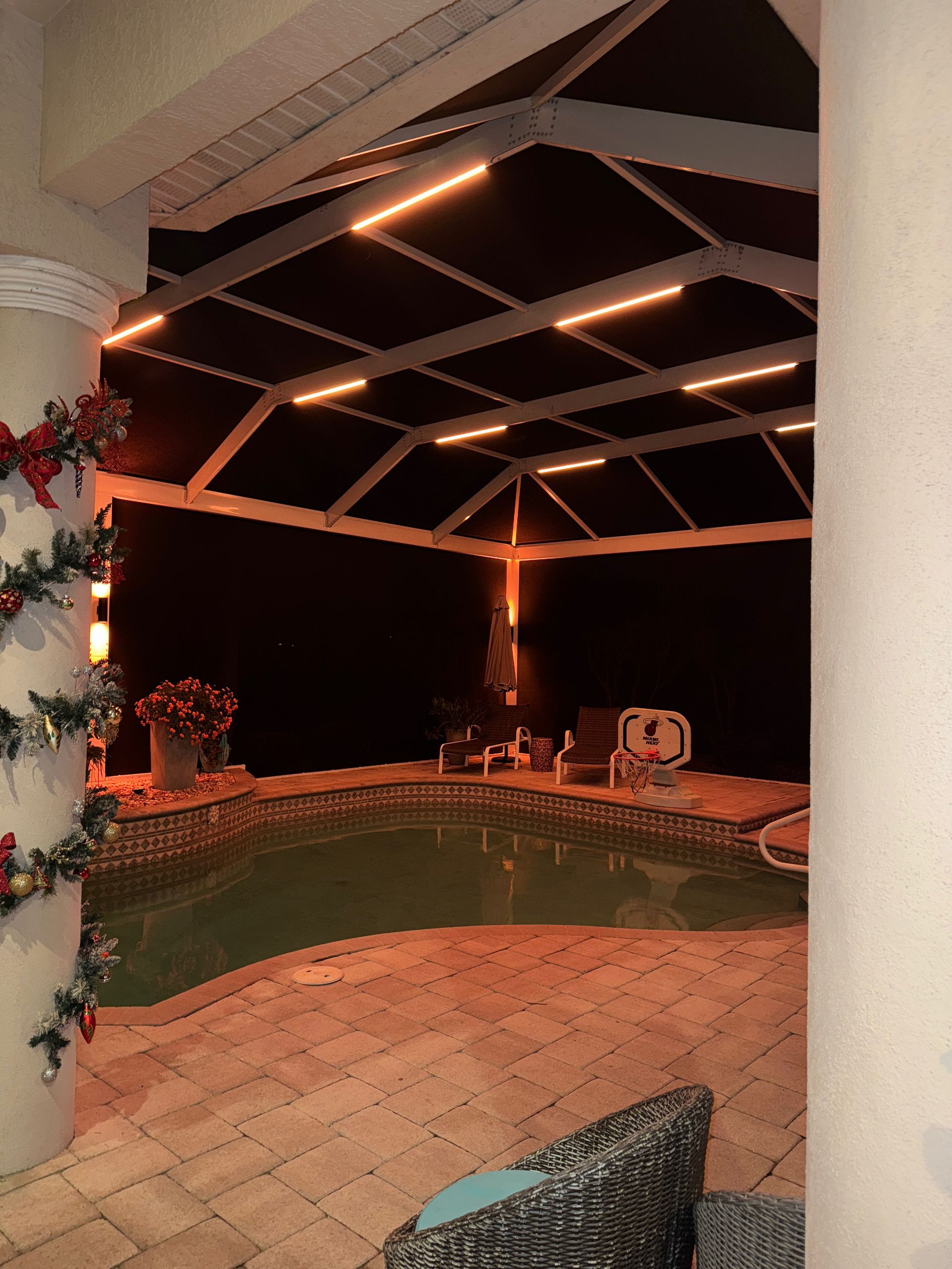 Poolside patio at night with orange lighting and Christmas decorations on a pillar.