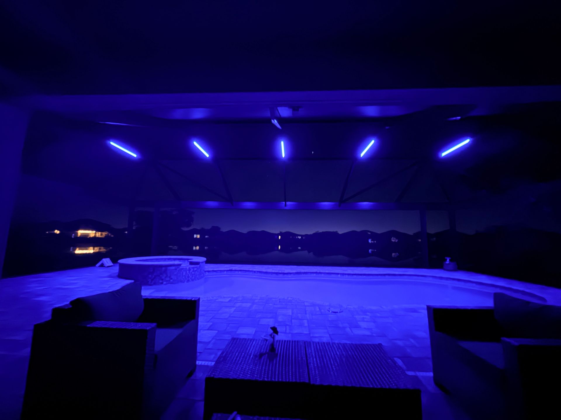 Outdoor patio at night, illuminated by blue lights. Includes seating area, with a dark background.