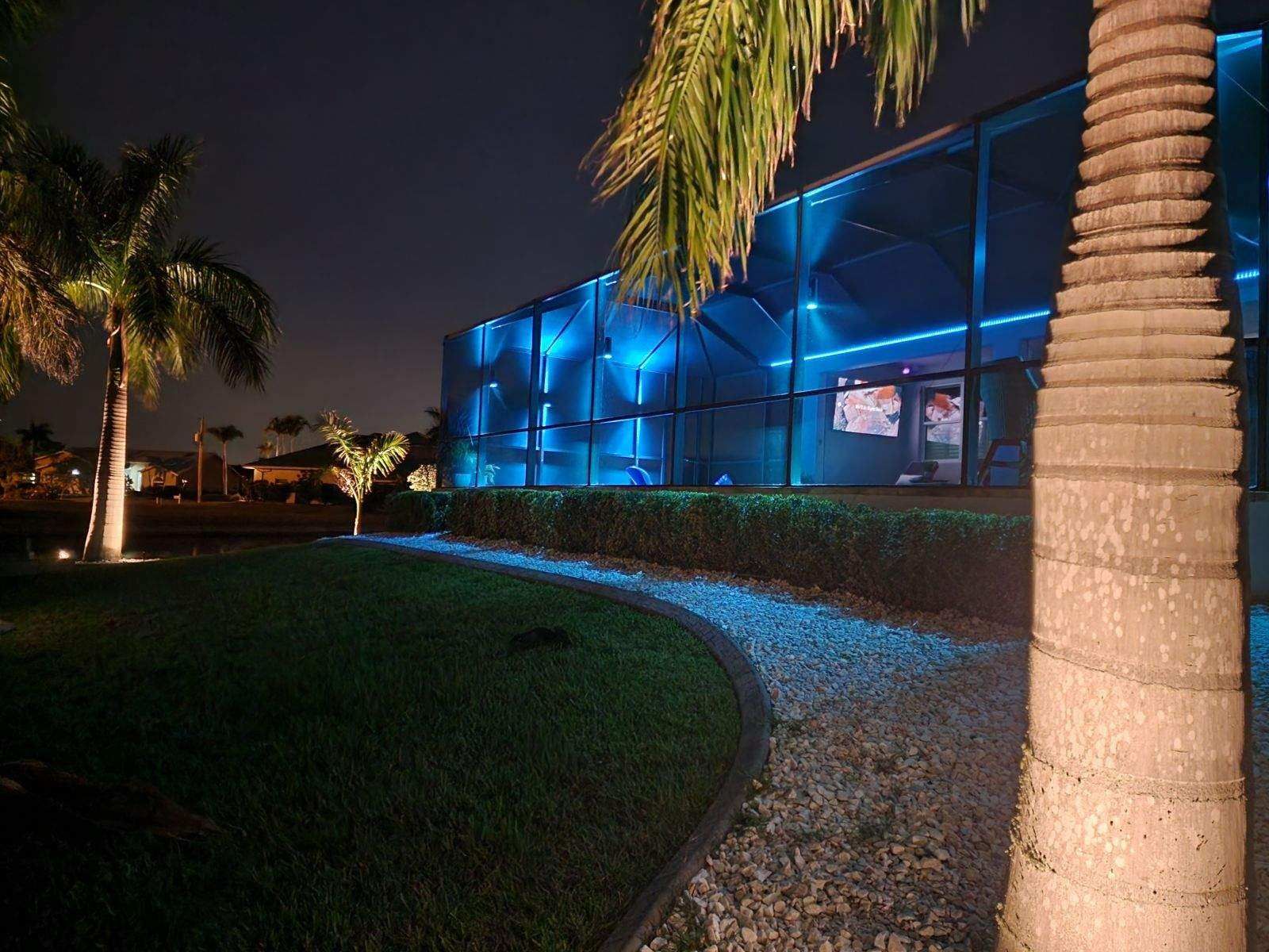 Screened-in patio with table and chairs, illuminated by overhead and wall lights at night.