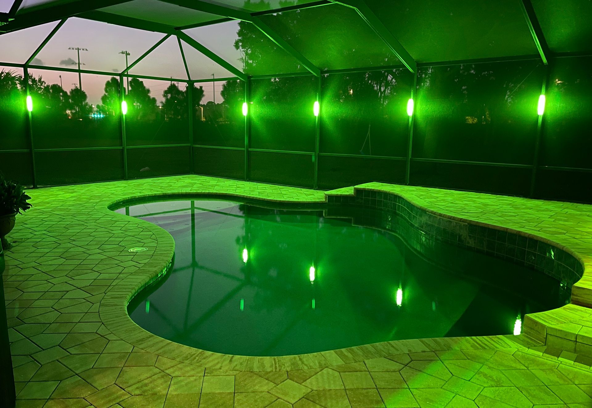 A pool lit with purple lights, enclosed in a screened patio at night.