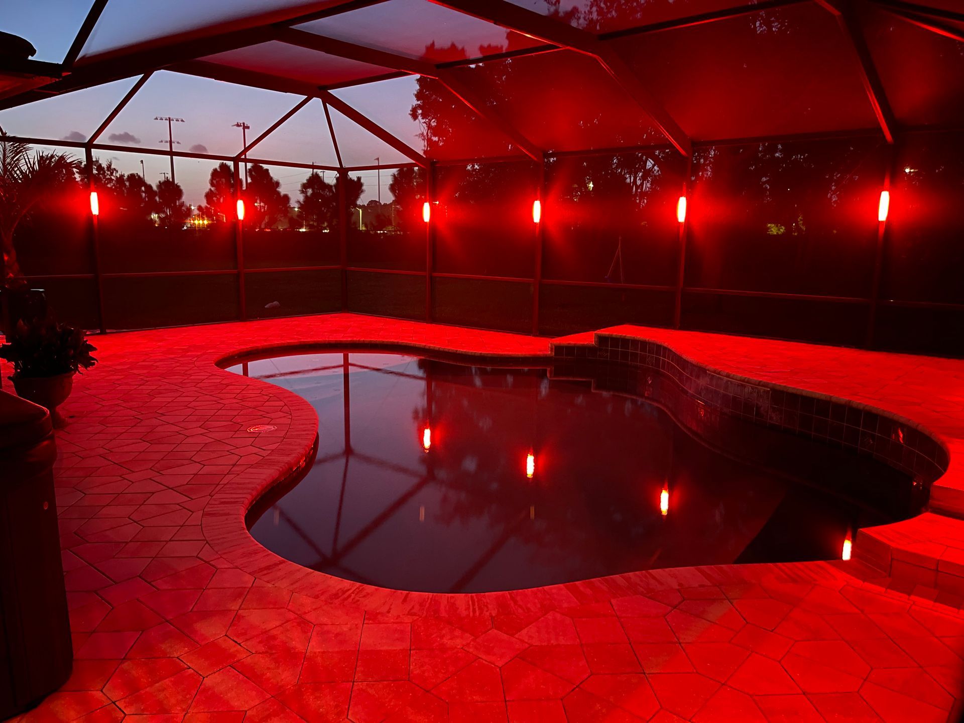 Red-lit pool at dusk with decorative torches around the perimeter.  Dark sky reflected in the water.
