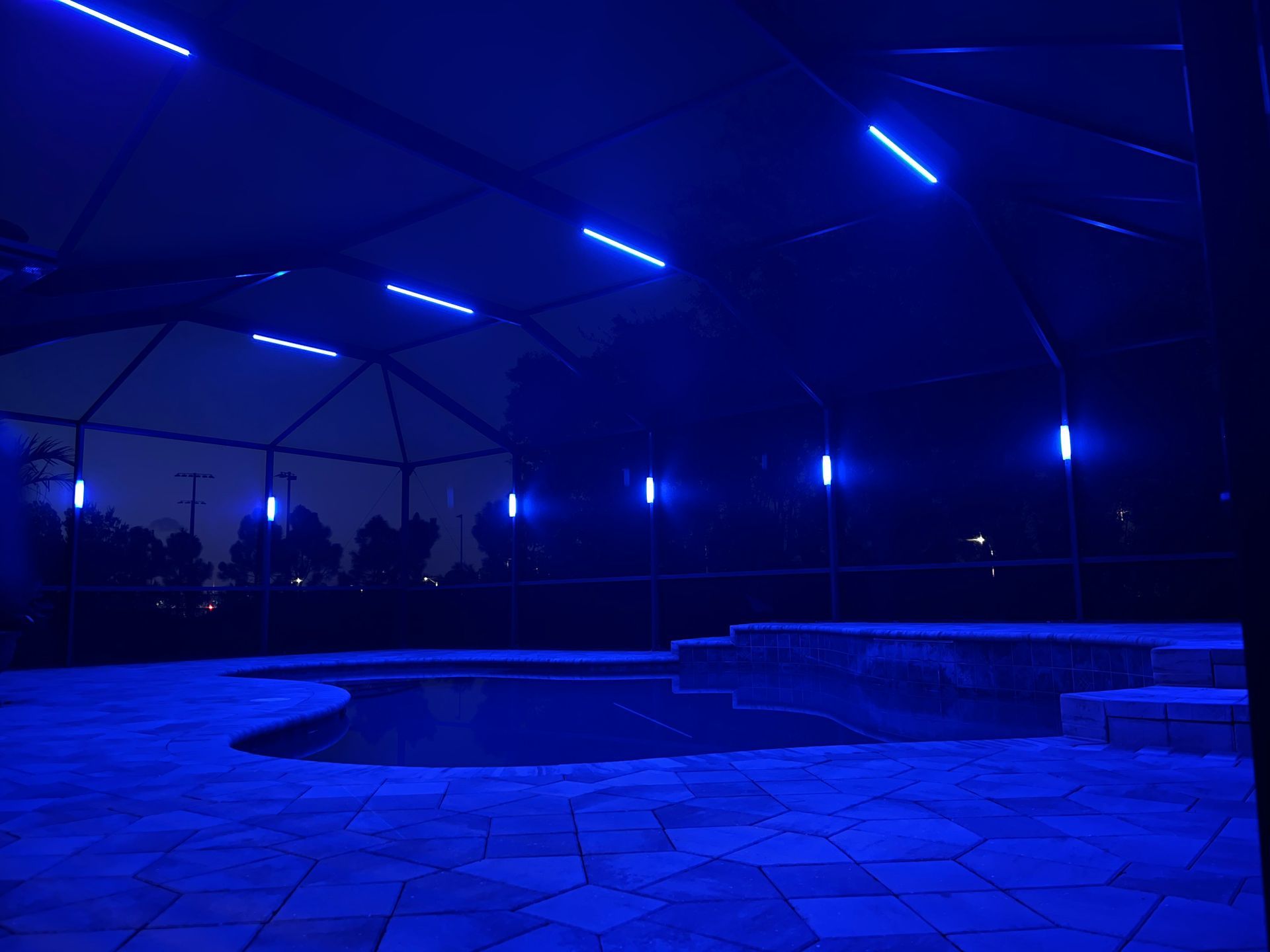 Blue illuminated pool at night under a covered patio. Outdoor lighting.